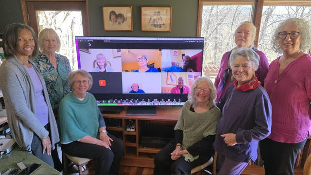 2025 Board of Directors standing together around Tv with other board members who attended remotely